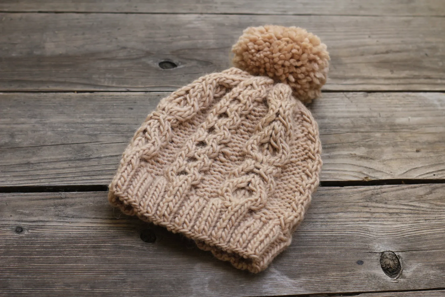 Knit beanie hat in beige color with cables and pom pom