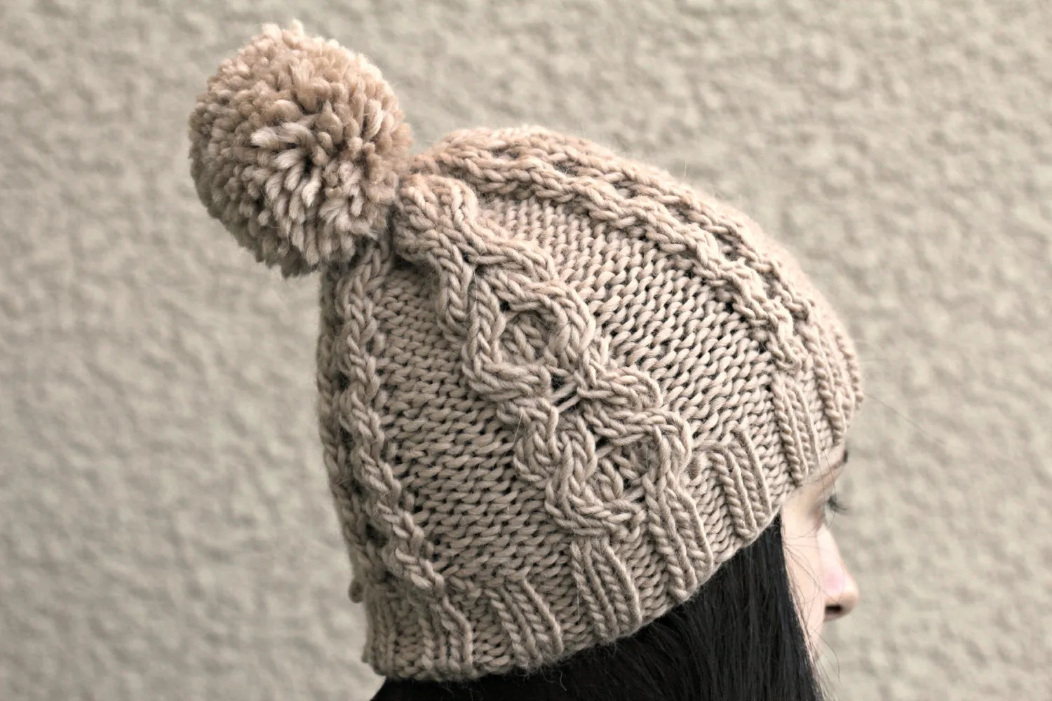 Knit beanie hat in beige color with cables and pom pom
